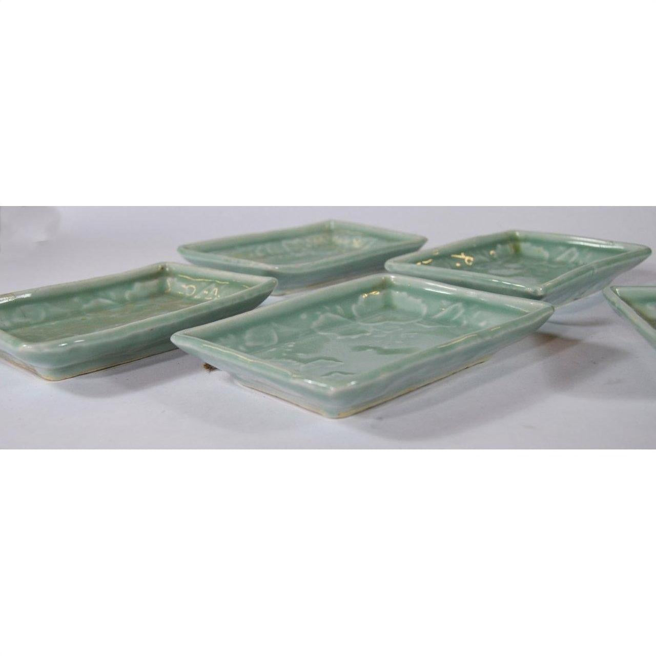 Close-up of five green Japanese Celadon ceramic serving bowls overlapping on a white surface.