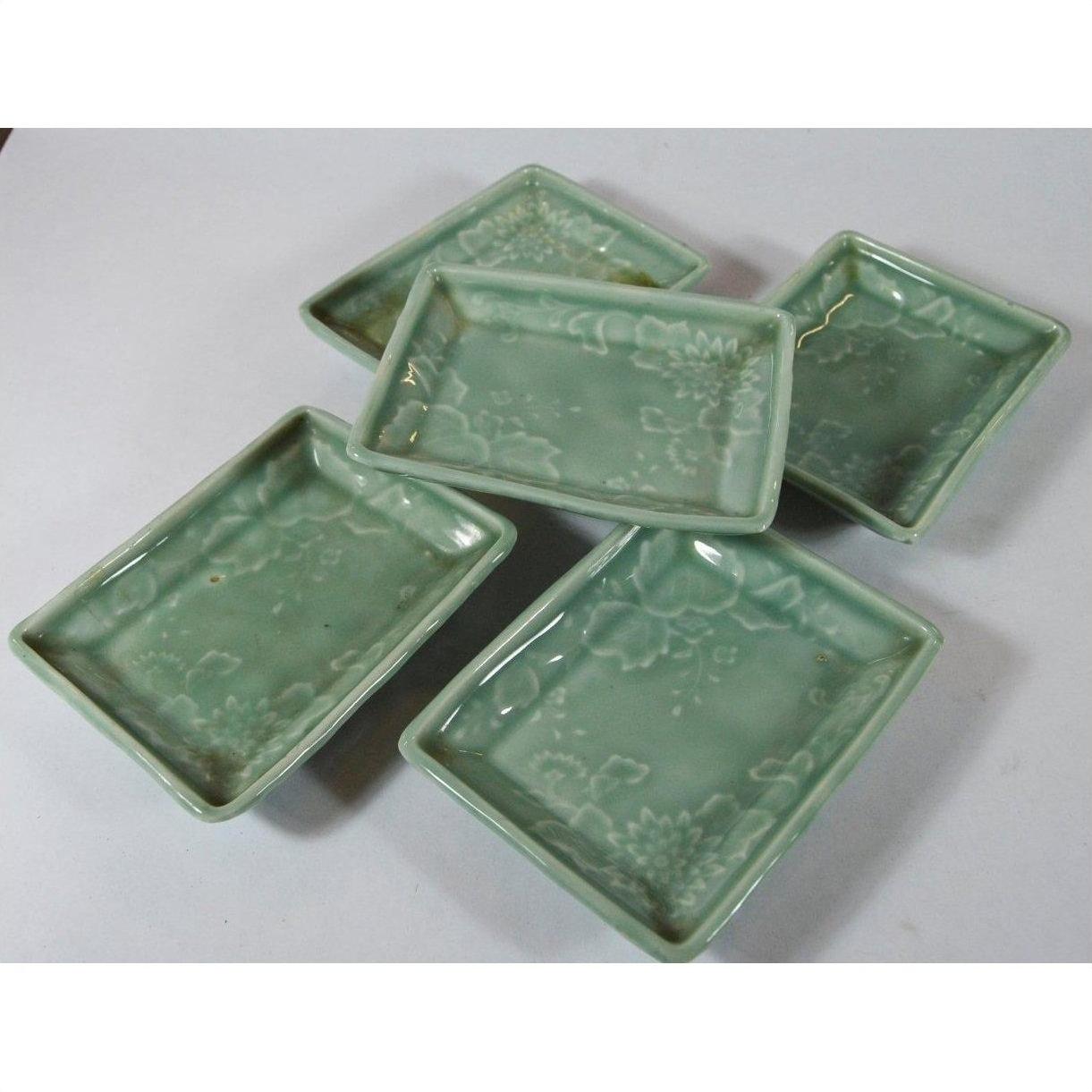 Green celadon ceramic Japanese serving bowls with floral patterns arranged on a white surface.