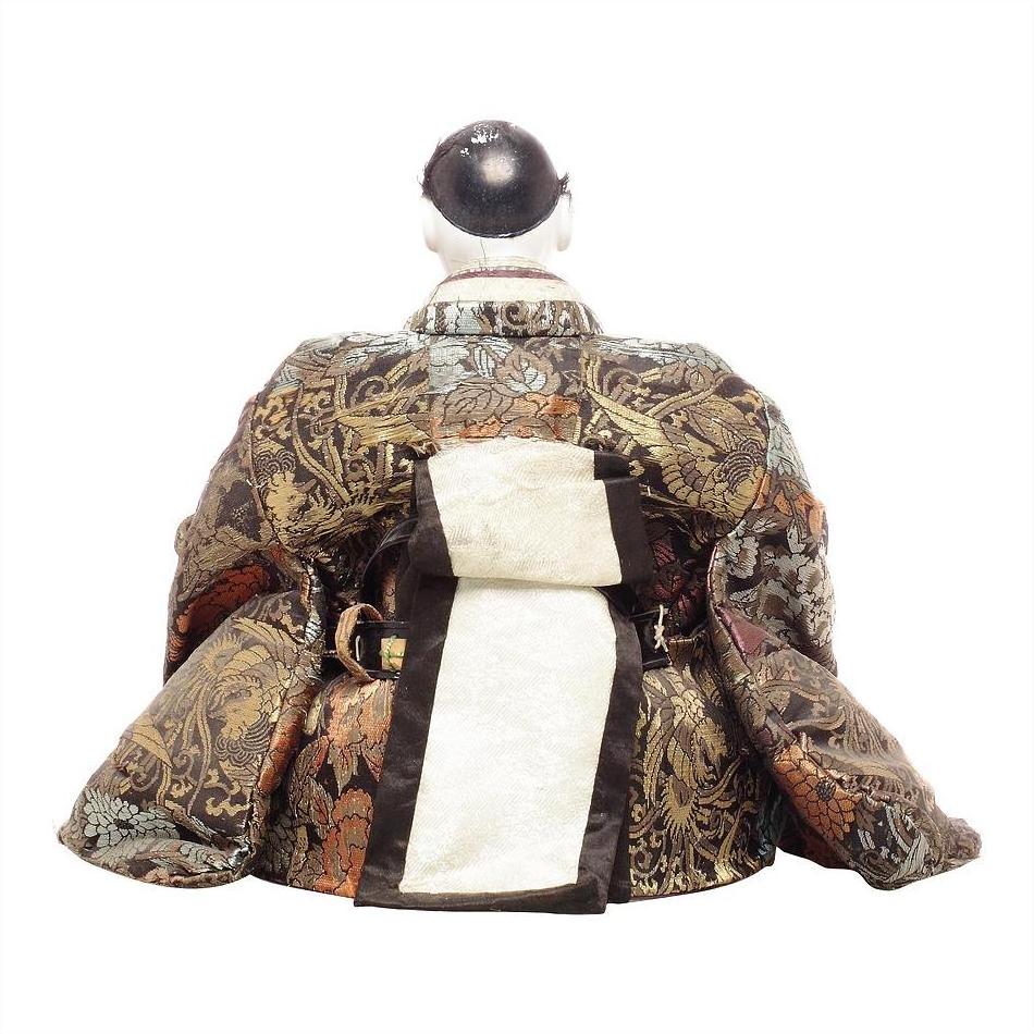 Close-up of Japanese doll in colorful patterned silk robe with large obi, rear view on white background.
