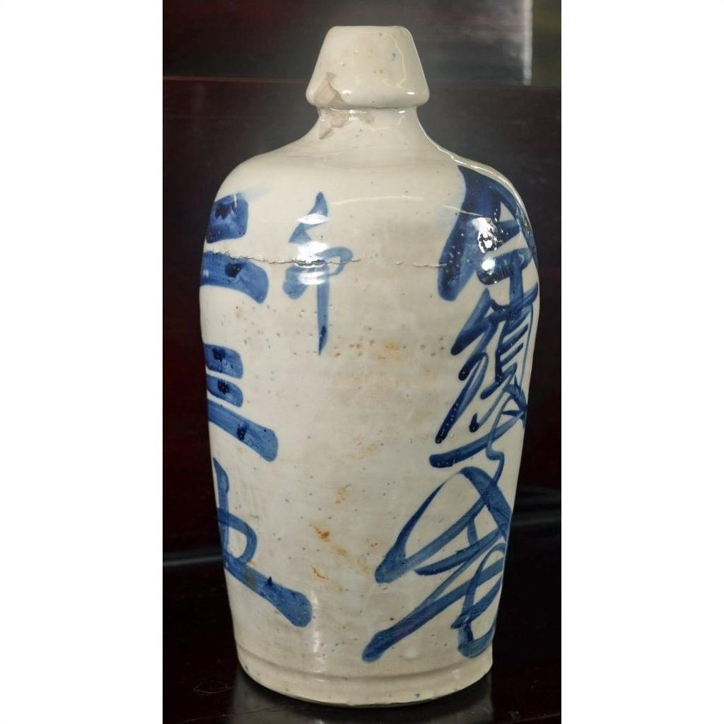 Close-up of a white ceramic Japanese doll with blue calligraphy, narrow neck, Kyoto-inspired design.
