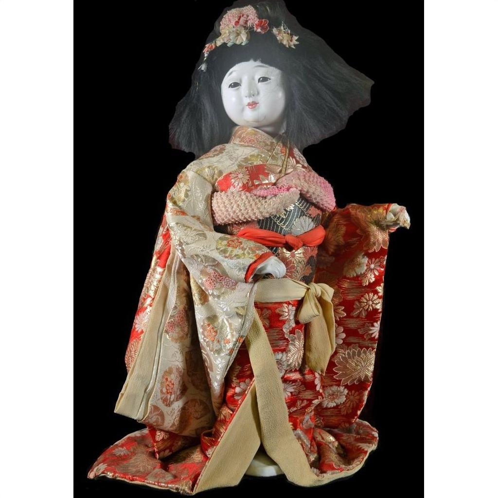 Close-up of an antique Japanese doll in a floral kimono and flower headdress against a black background.