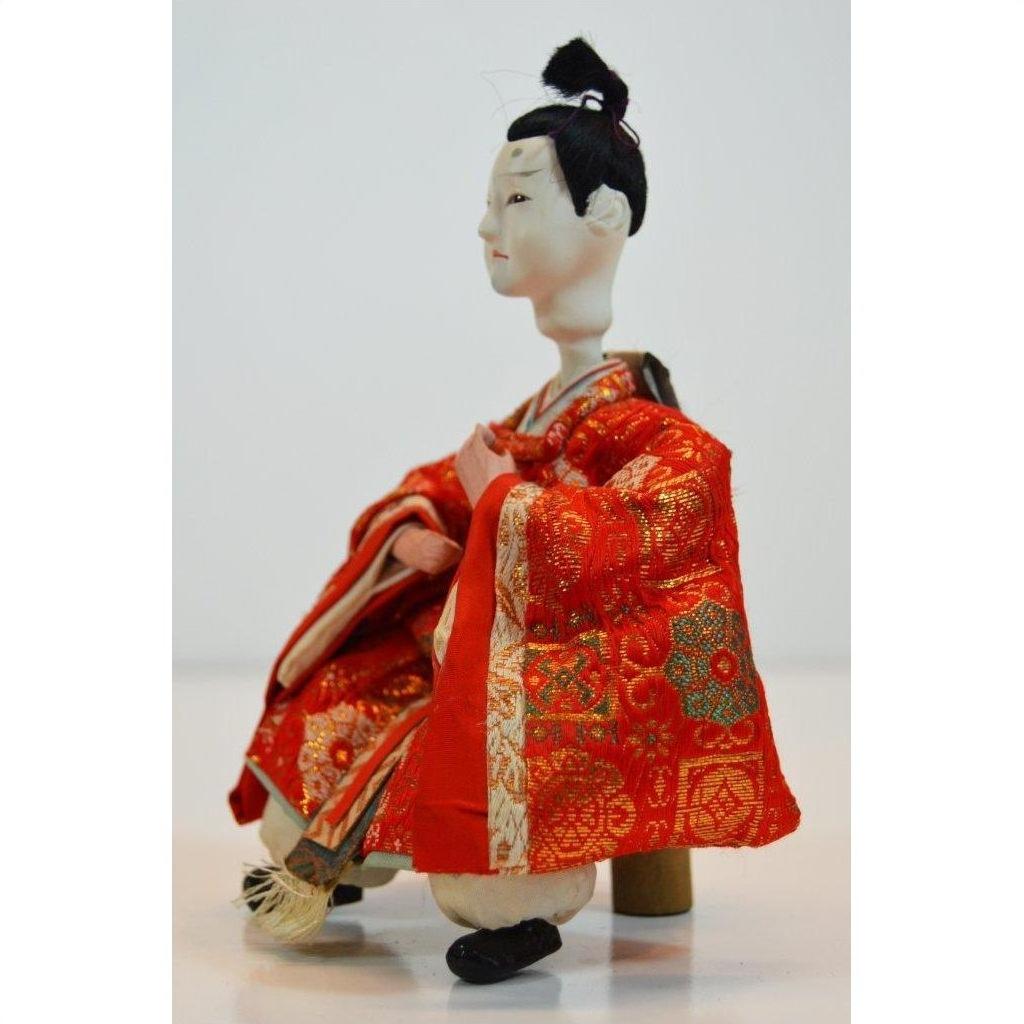 Red and gold kimono Japanese doll with styled black hair, seated, Kyoto-made, close-up.