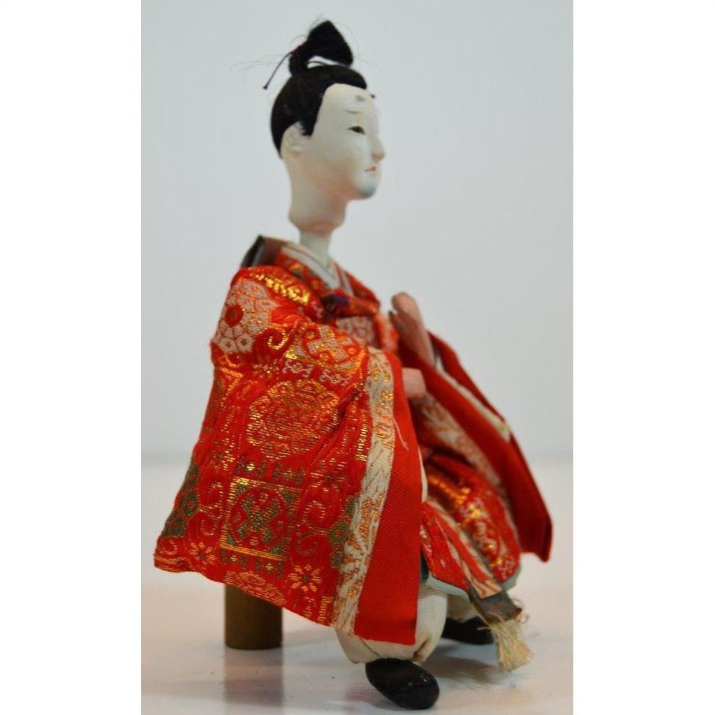 Red patterned fabric Japanese doll on wooden stool, plain background, Kyoto-made, close-up product view.