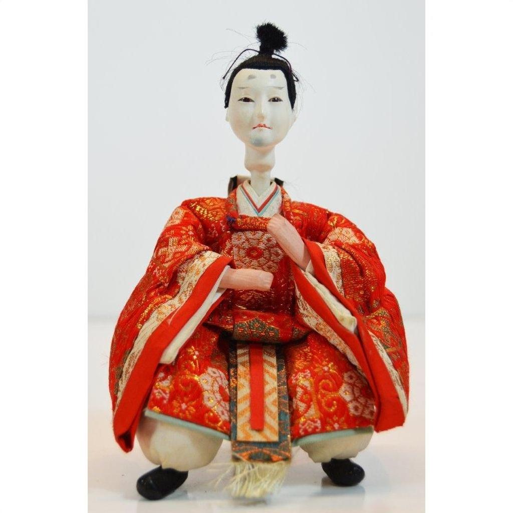 Close-up of a Kyoto-made Japanese doll in an ornate red kimono, seated with hands placed gracefully in front.
