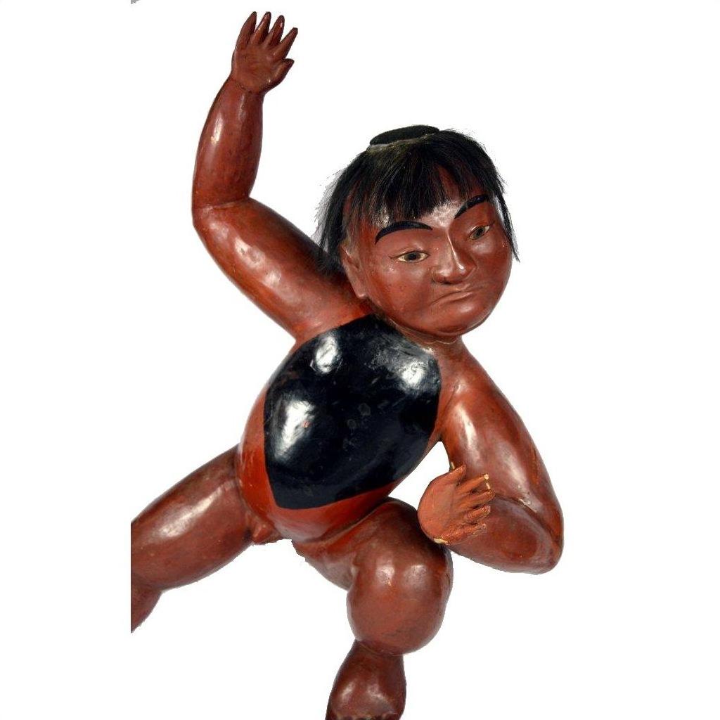 Brown wooden hand-carved Japanese lacquered boy figure with black hair and chest patch, raised arms, close-up.