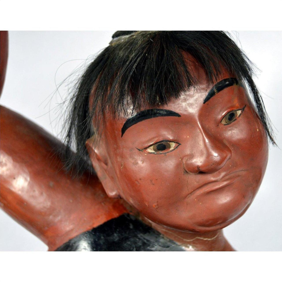 Close-up of hand-carved lacquered Japanese boy figurine with black hair, strong eyebrows, and expressive face.