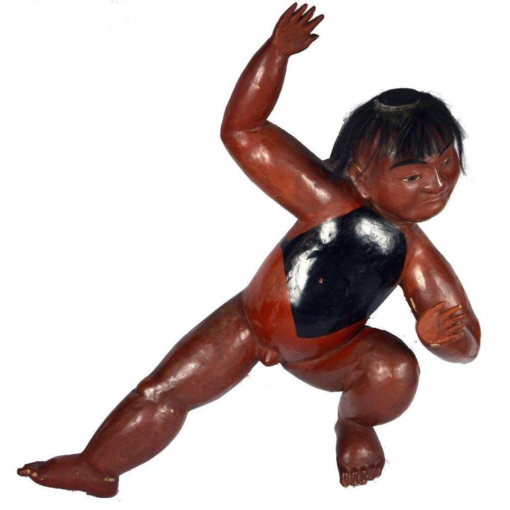 Close-up of Japanese hand-carved lacquered boy figurine with black hair, chest mark, and one arm raised.