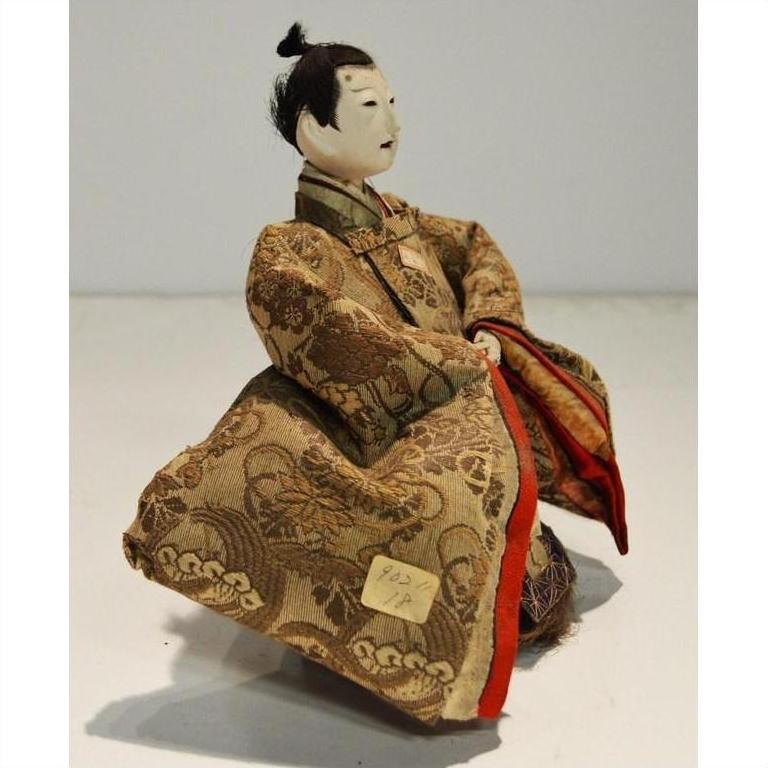 White-faced Japanese Taisho samurai doll in ornate robe, seated with folded arms, close-up view.
