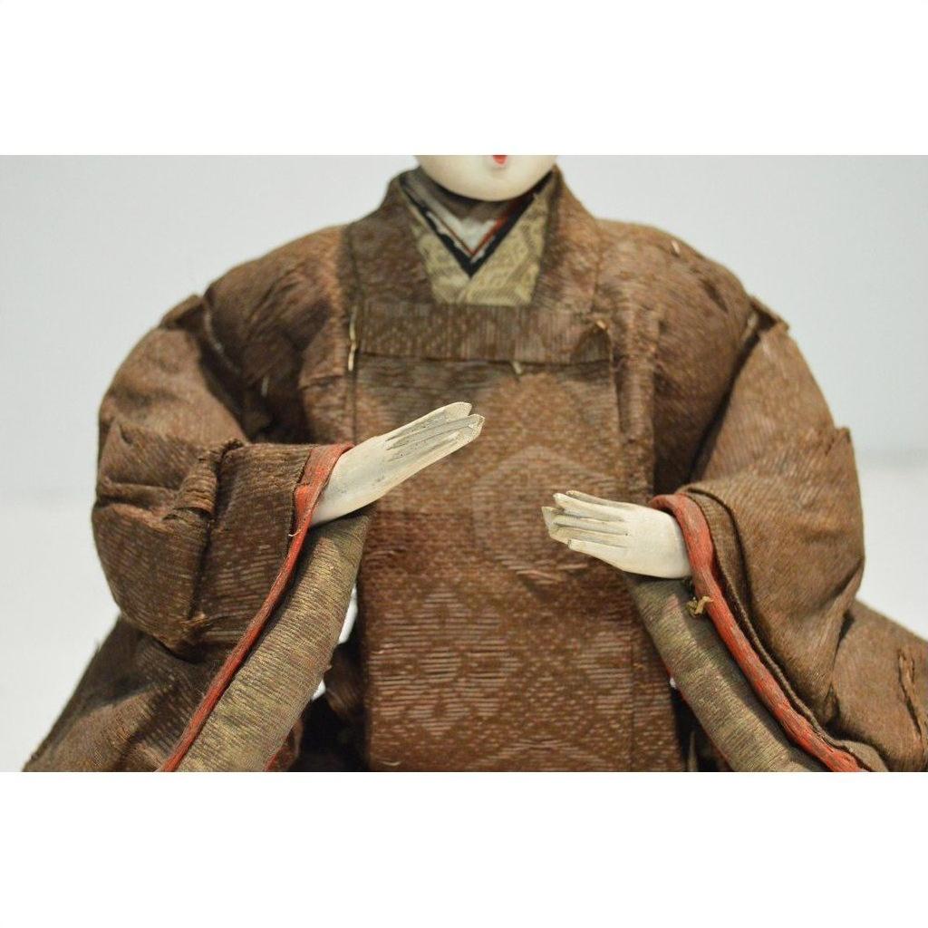 Close-up of a Japanese Taisho samurai doll wearing a brown kimono, hands positioned in front.