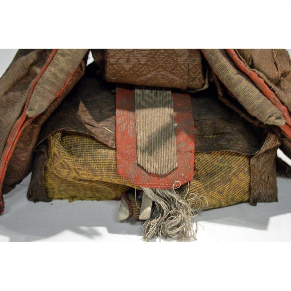 Close-up of a worn fabric bundle with frayed edges and red-brown strap from a Japanese Taisho Samurai Doll.