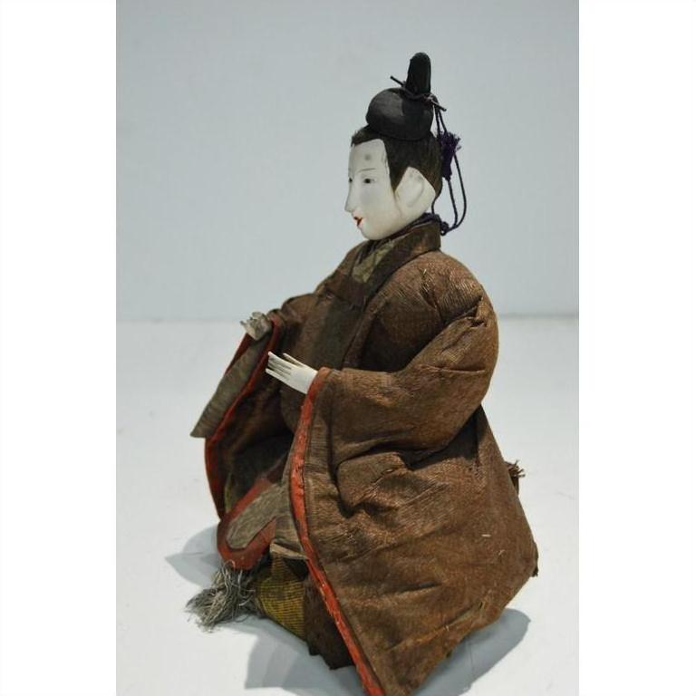 Brown fabric samurai doll with black hair ornament, seated with hands raised, indoors.