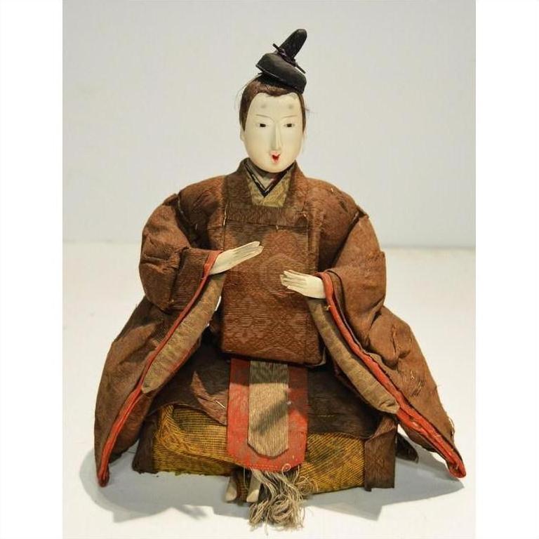 Close-up of Japanese Taisho Samurai doll in brown kimono, seated with folded hands and small hat, fabric details visible.