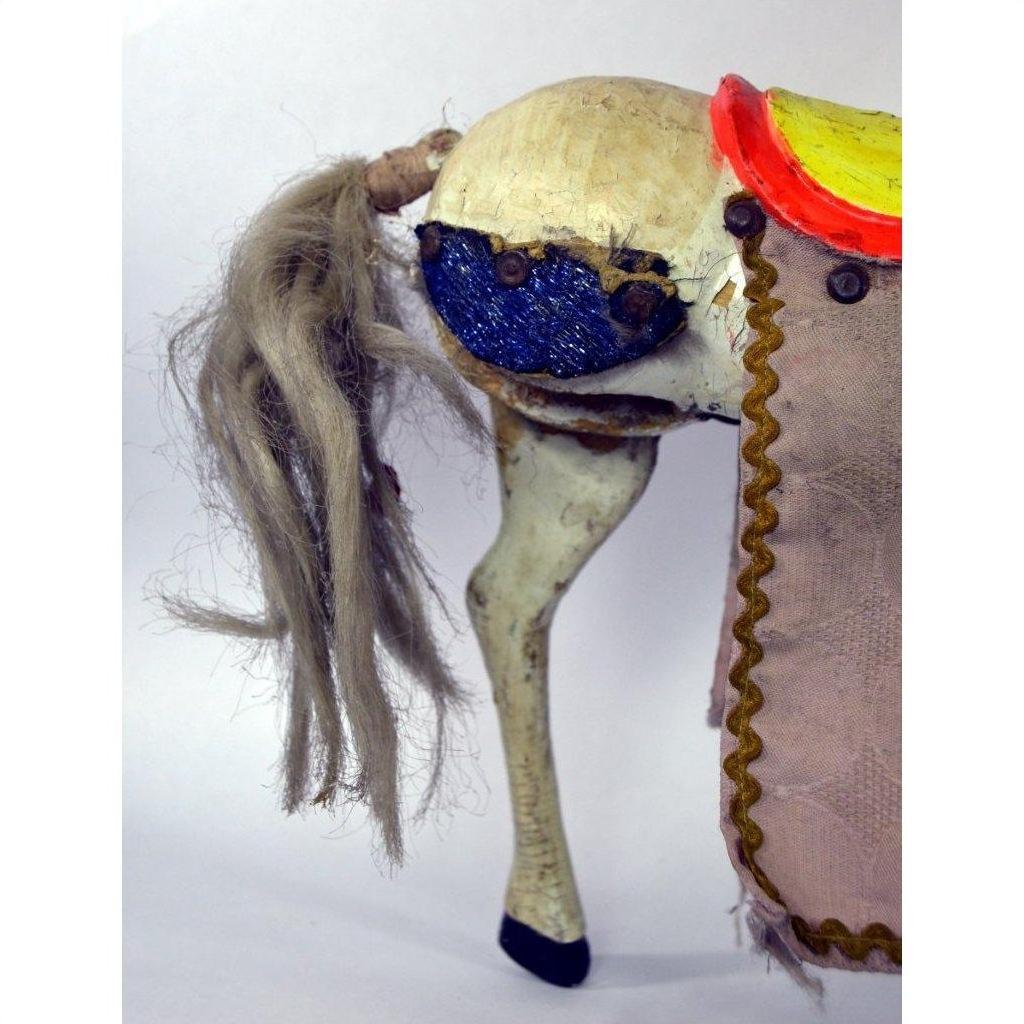 Close-up of a handmade Japanese two-headed horse toy with yarn tail, blue eye, and fabric saddle on white background.