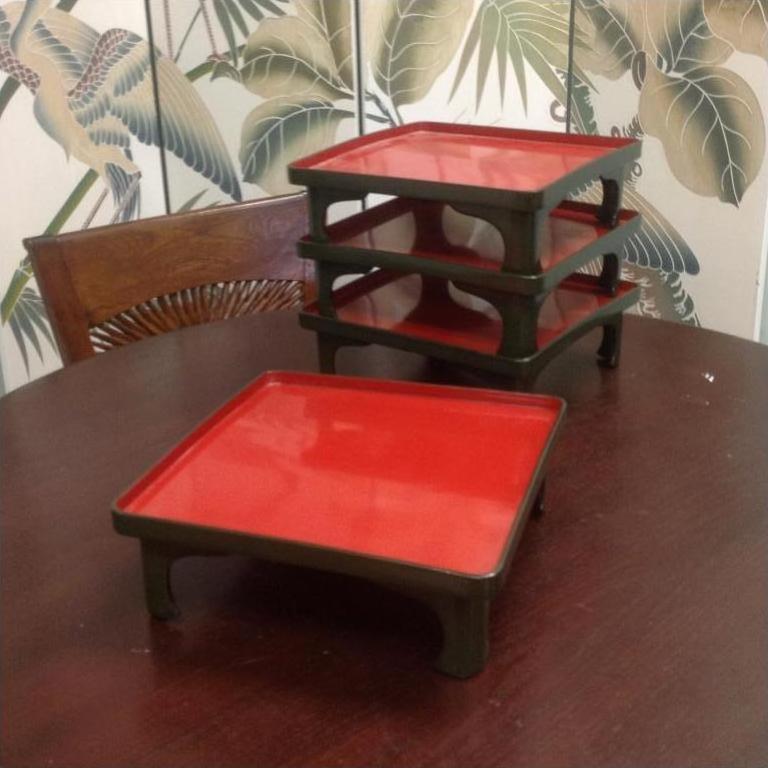 Red and black Japanese Urushi lacquered trays stacked on dark wood table, one tray set aside, close-up.