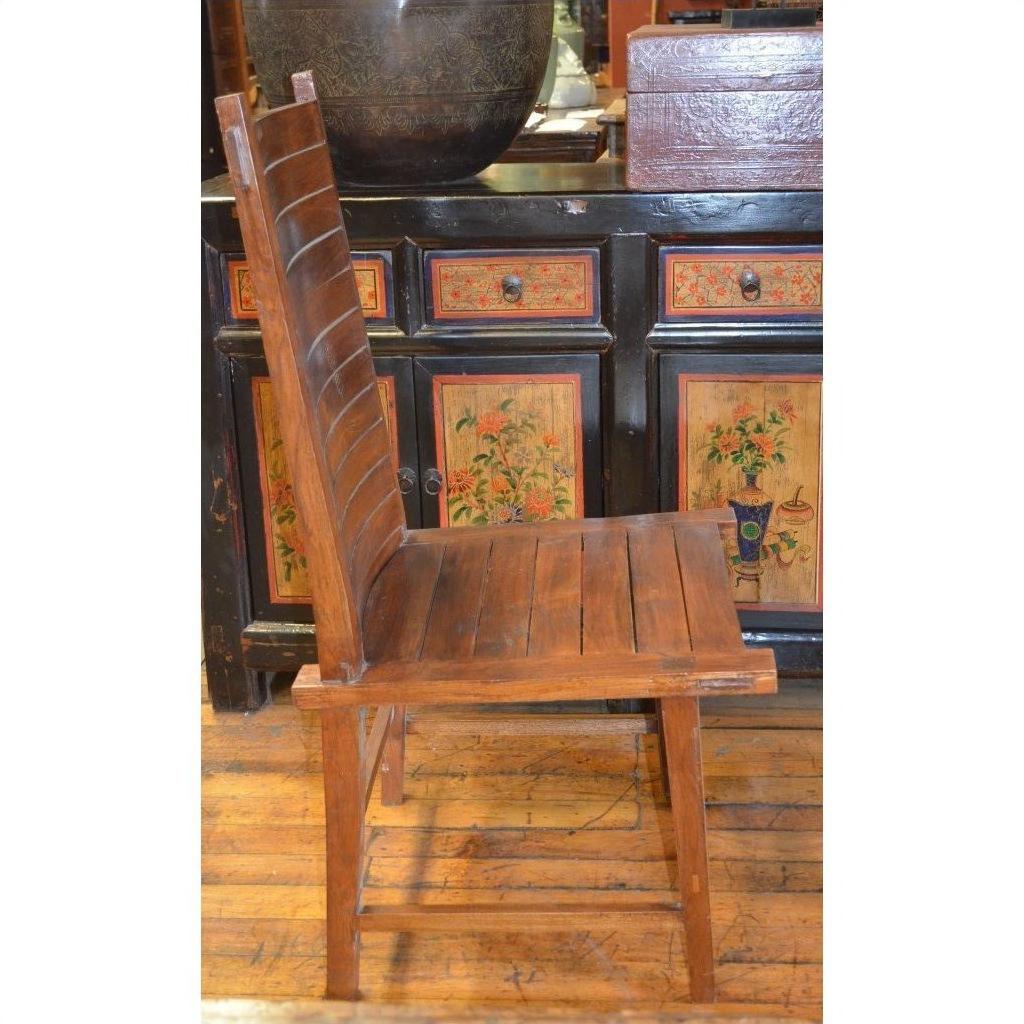 Brown teak wood side chair with high slatted back on wooden floor, positioned in front of a painted cabinet.
