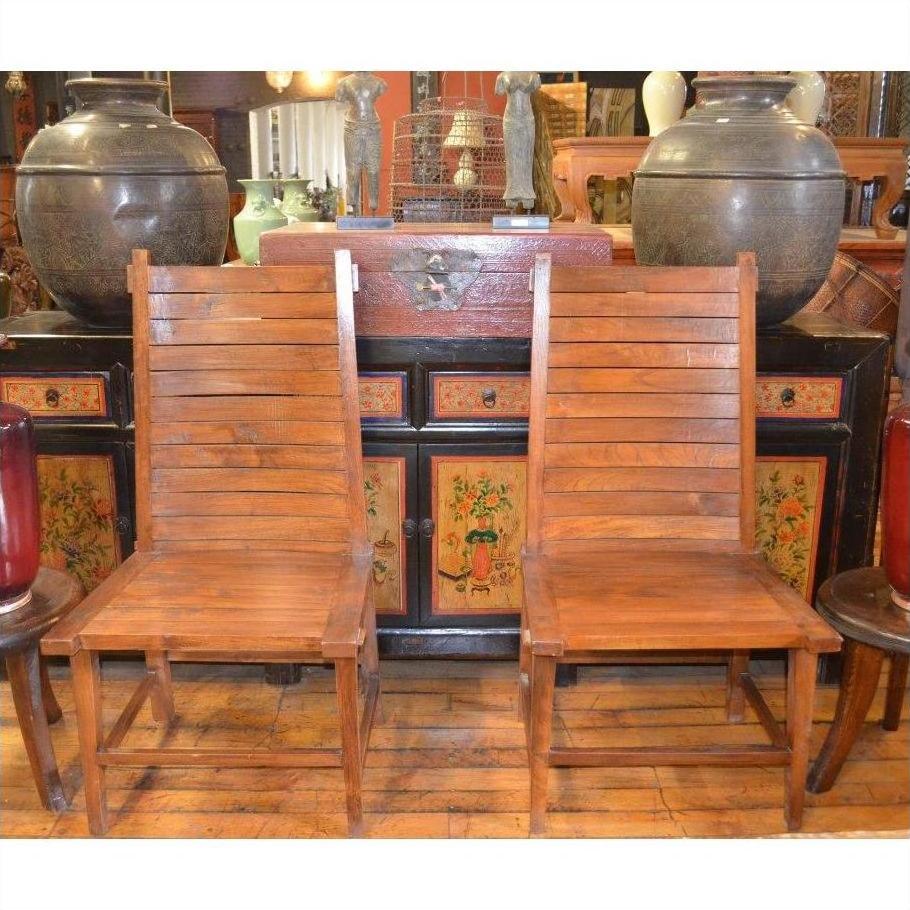 Brown teak wood side chairs beside each other in front of a vintage cabinet with painted floral details and vases indoors.
