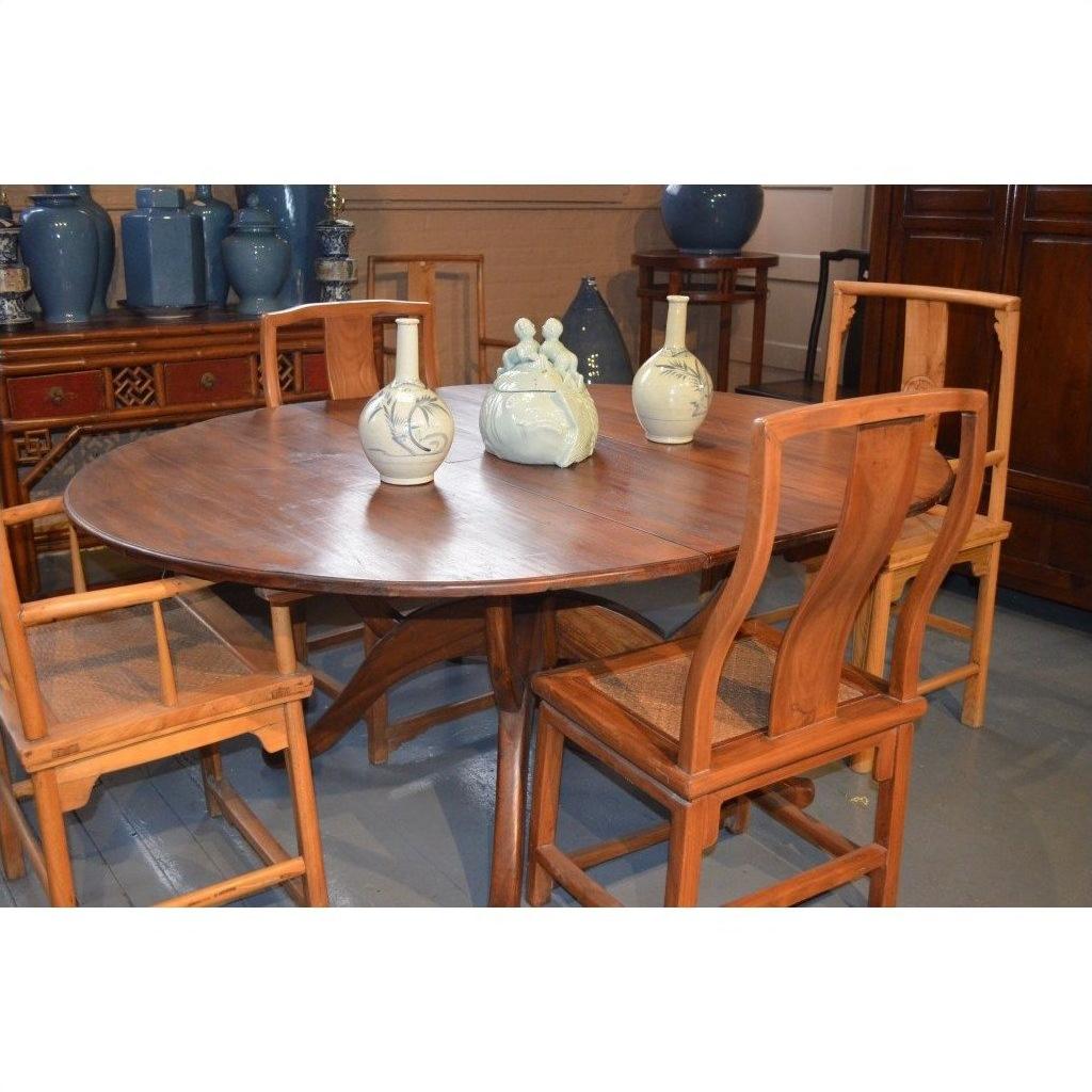 Brown wood Javanese oval dining table with leaf and four matching chairs, styled with decorative blue vases in background.