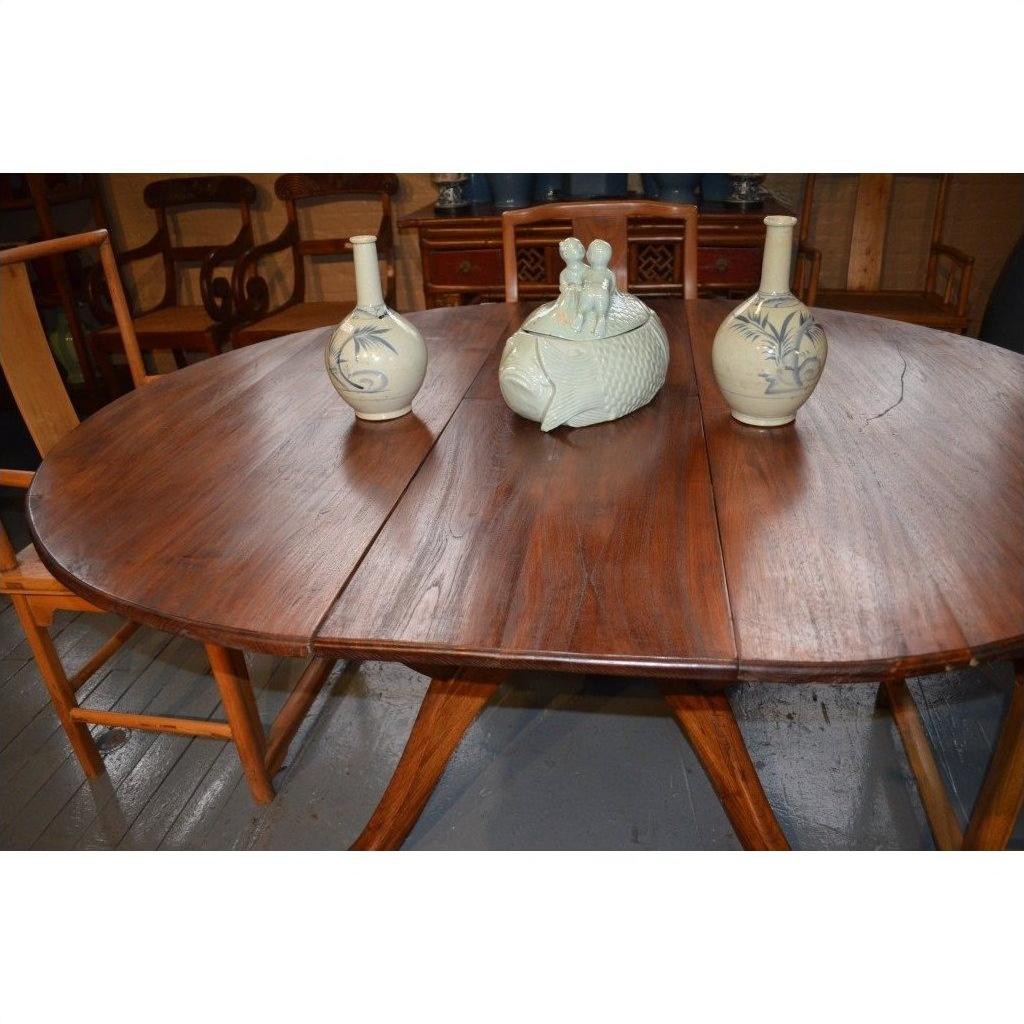 Brown wood Javanese oval dining table with leaf, three ceramic vases, animal pottery centerpiece, wooden chairs around.