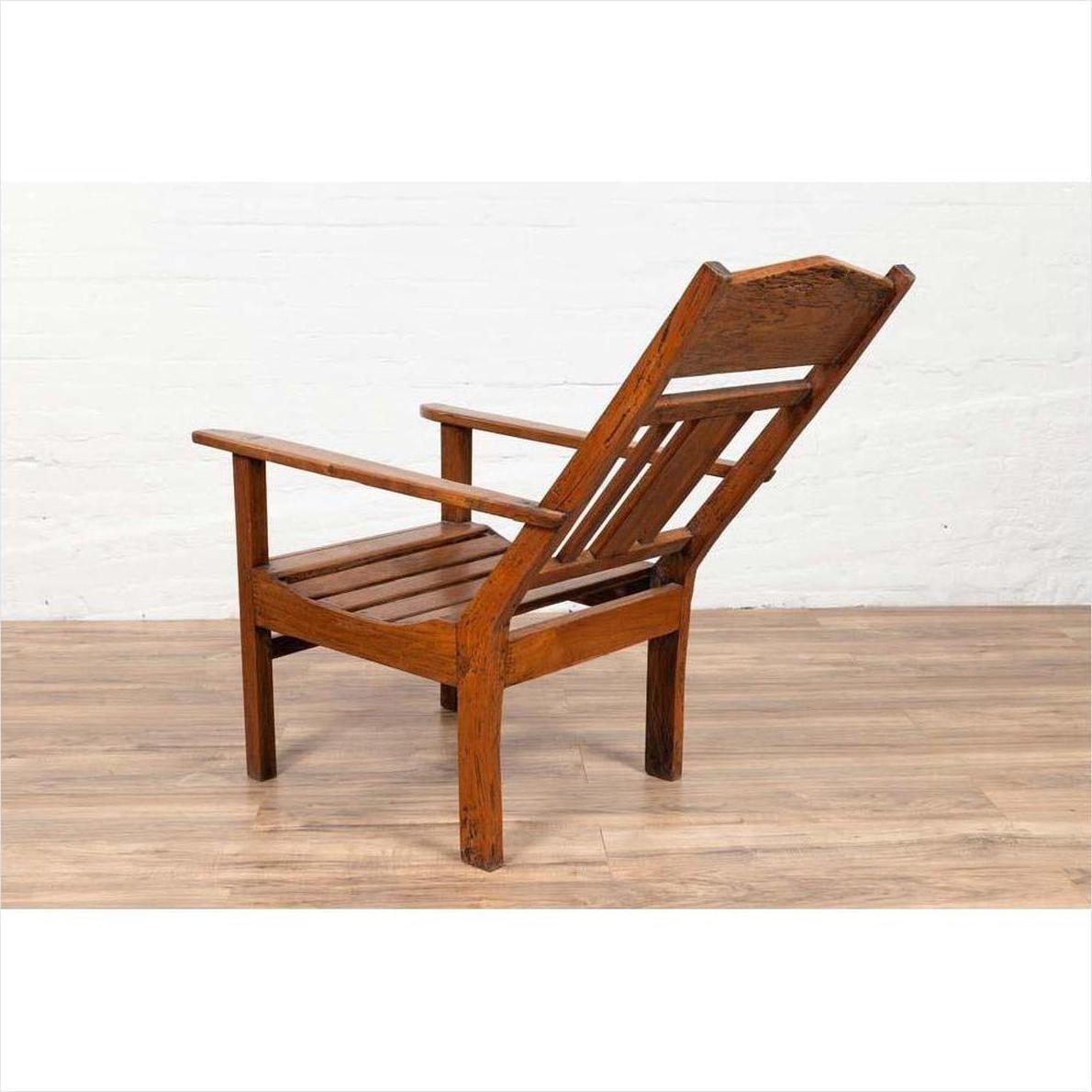 Brown wood lounge chair with slanted back on a wooden floor against a white wall indoors.