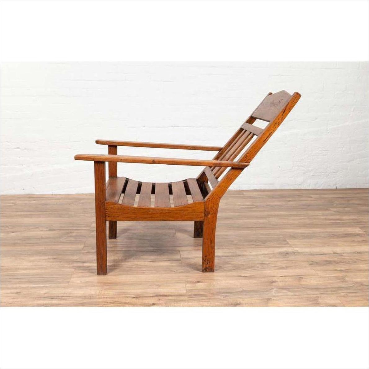 Brown wooden lounge chair with slanted back, side view on wood floor against white wall.