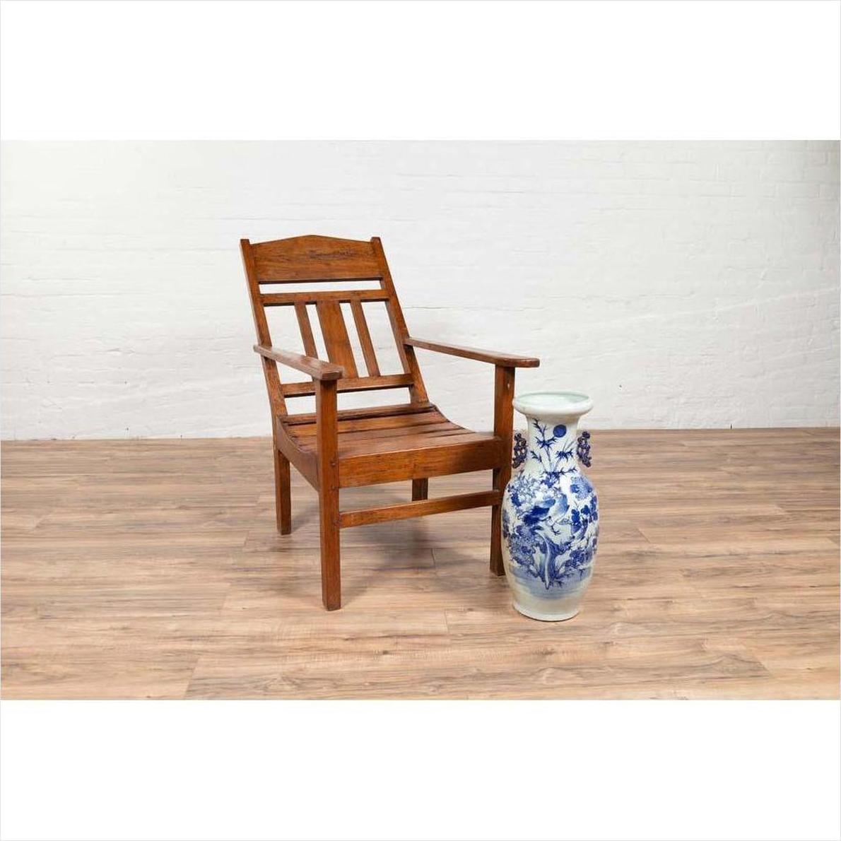 Brown wooden lounge chair with slanted back on wooden floor next to blue floral ceramic vase indoors.