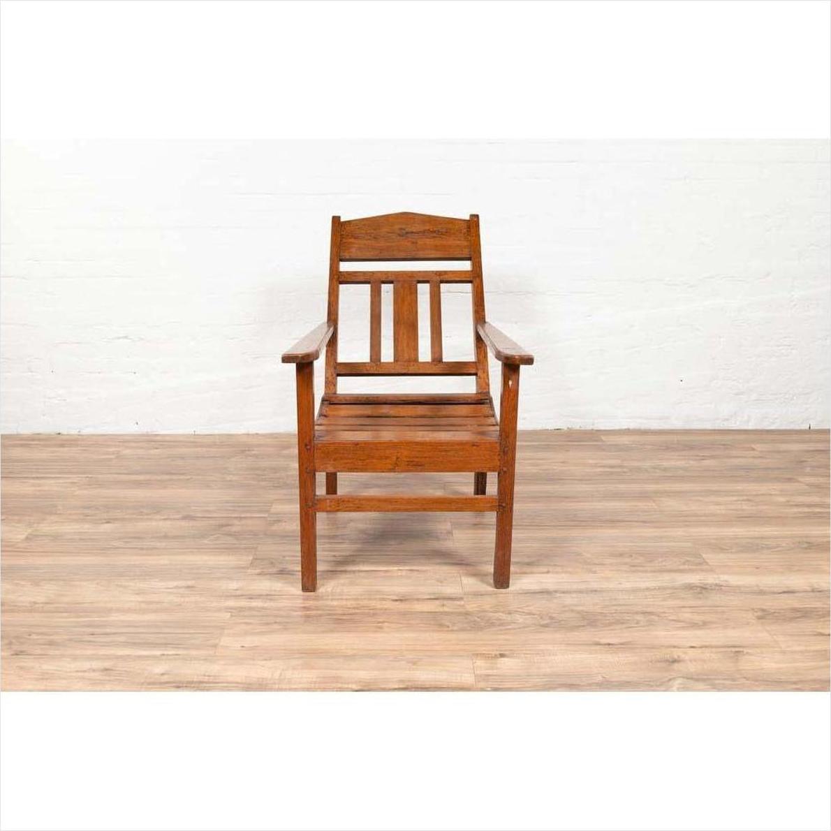 Brown wooden lounge chair with slanted back on light wood floor against a white wall indoors.