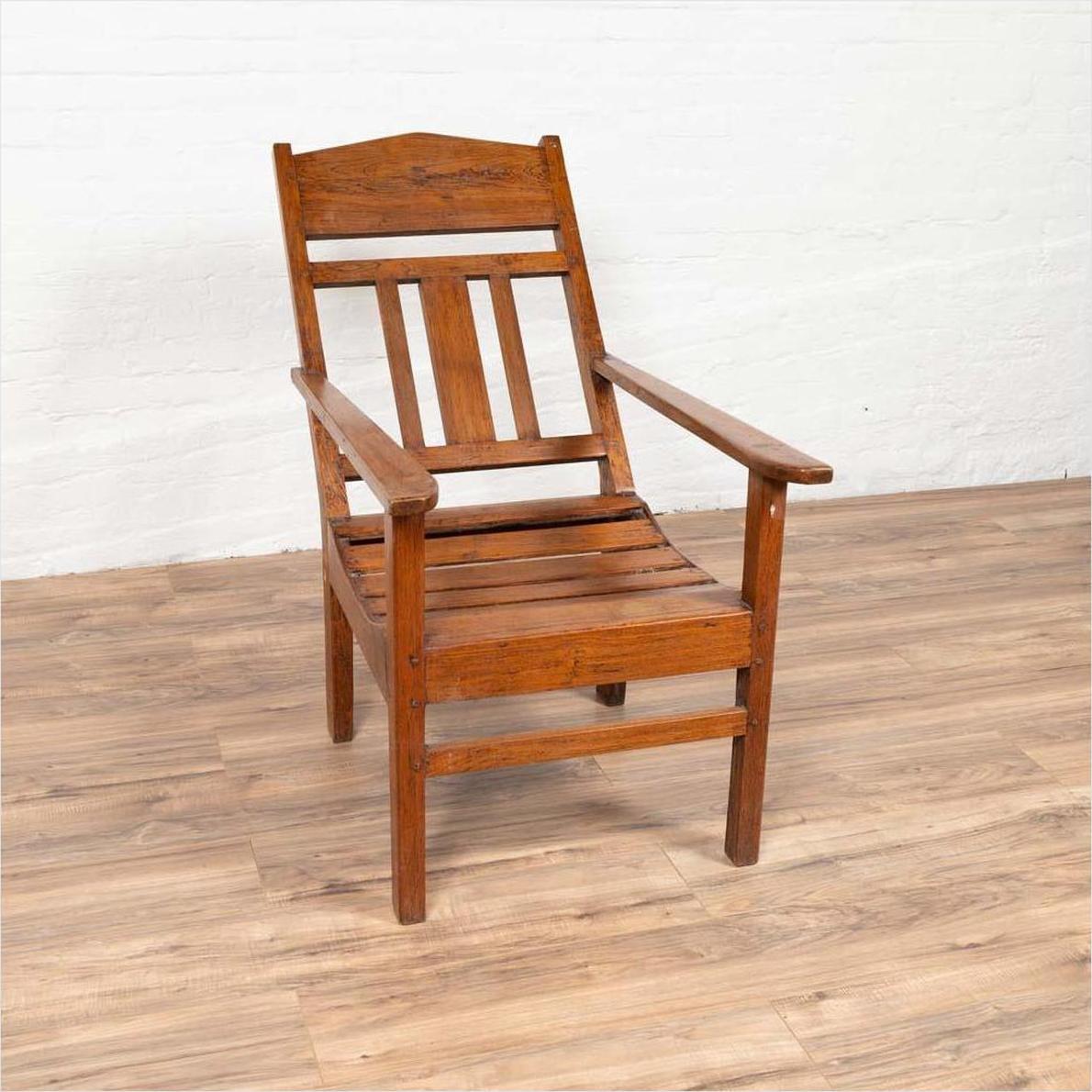Brown wood lounge chair with slanted back on light wood floor against a white wall, indoors.
