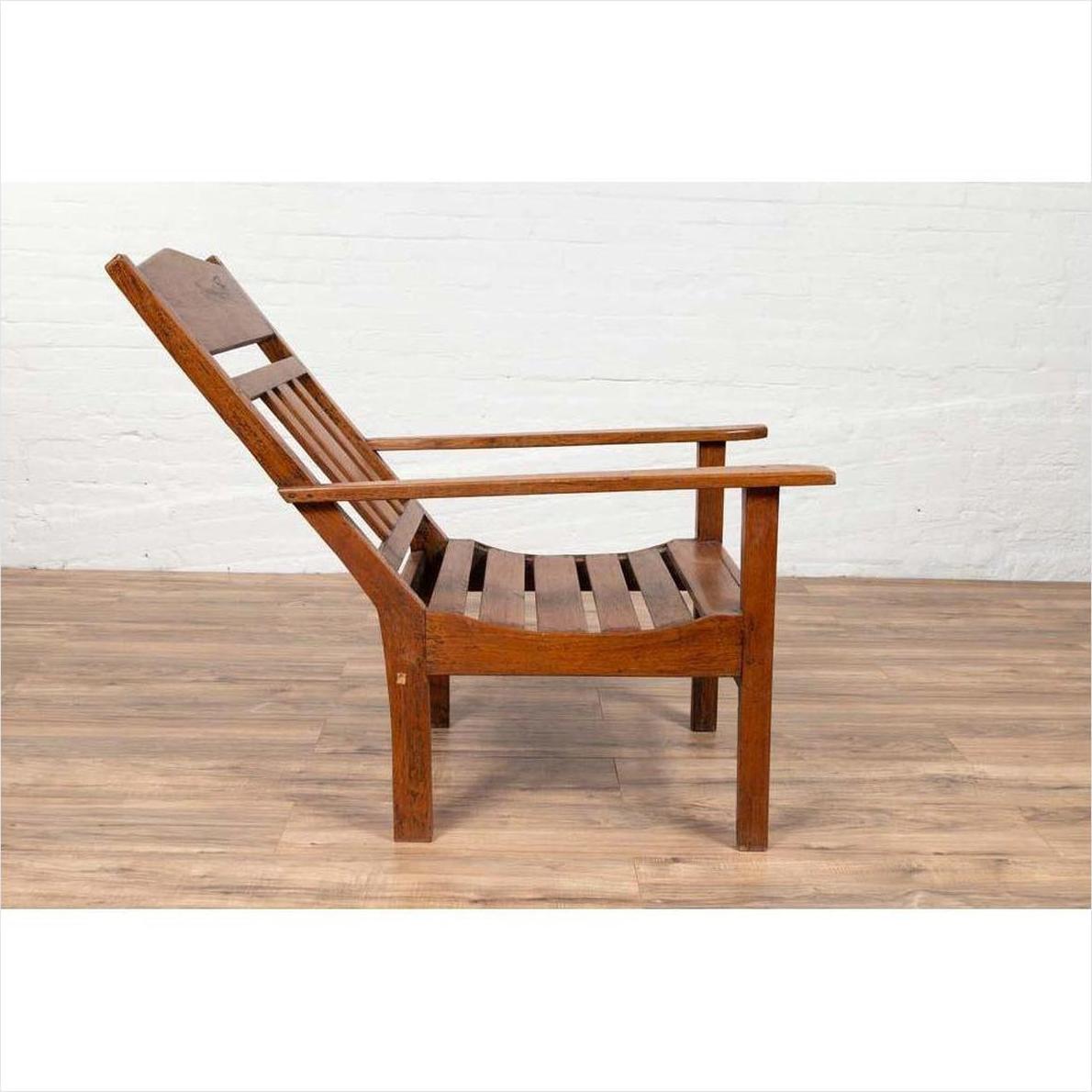 Brown wooden lounge chair with slanted back on wooden floor next to white brick wall indoors.