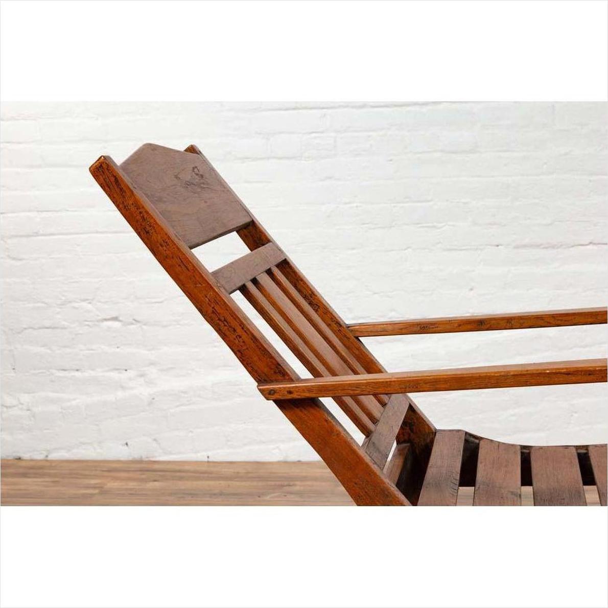 Brown wooden lounge chair with slanted back, placed indoors against a white brick wall and wooden floor.