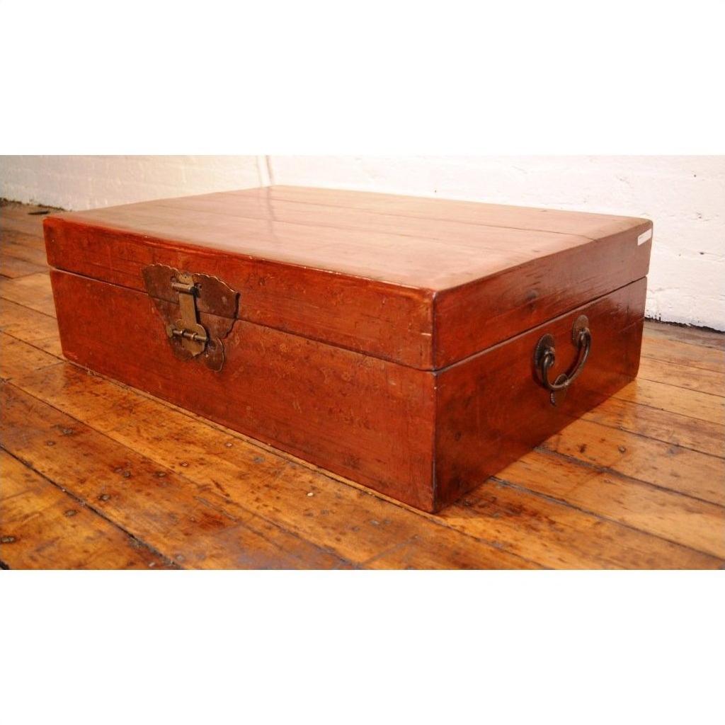 Black lacquer leather trunk with butterfly hardware and metal handles on a polished wooden floor.