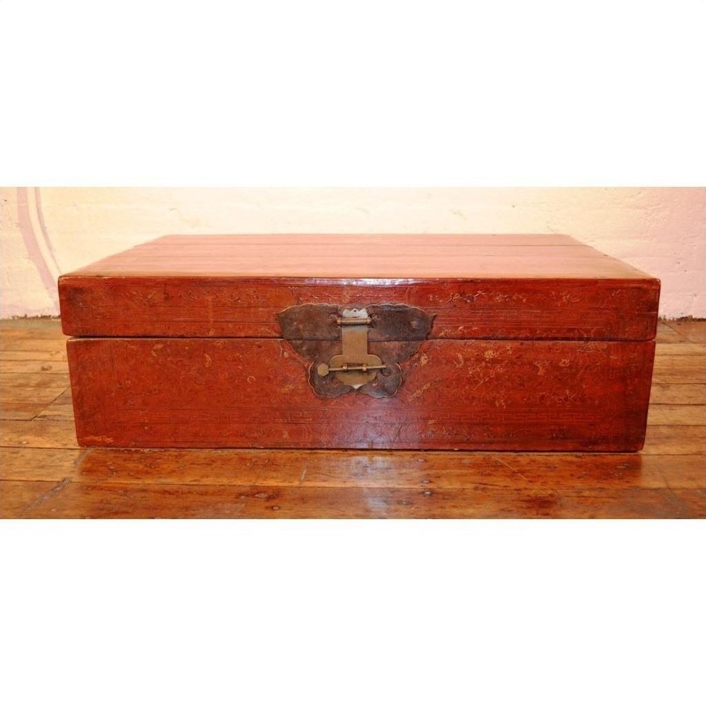 Black lacquer leather trunk with butterfly hardware on a wooden floor against a light-colored wall.