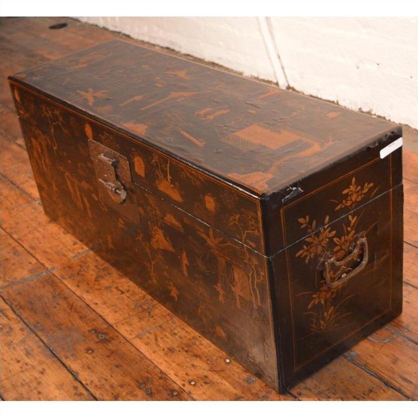 Black lacquer trunk with metal handles and painted designs on a wooden floor.