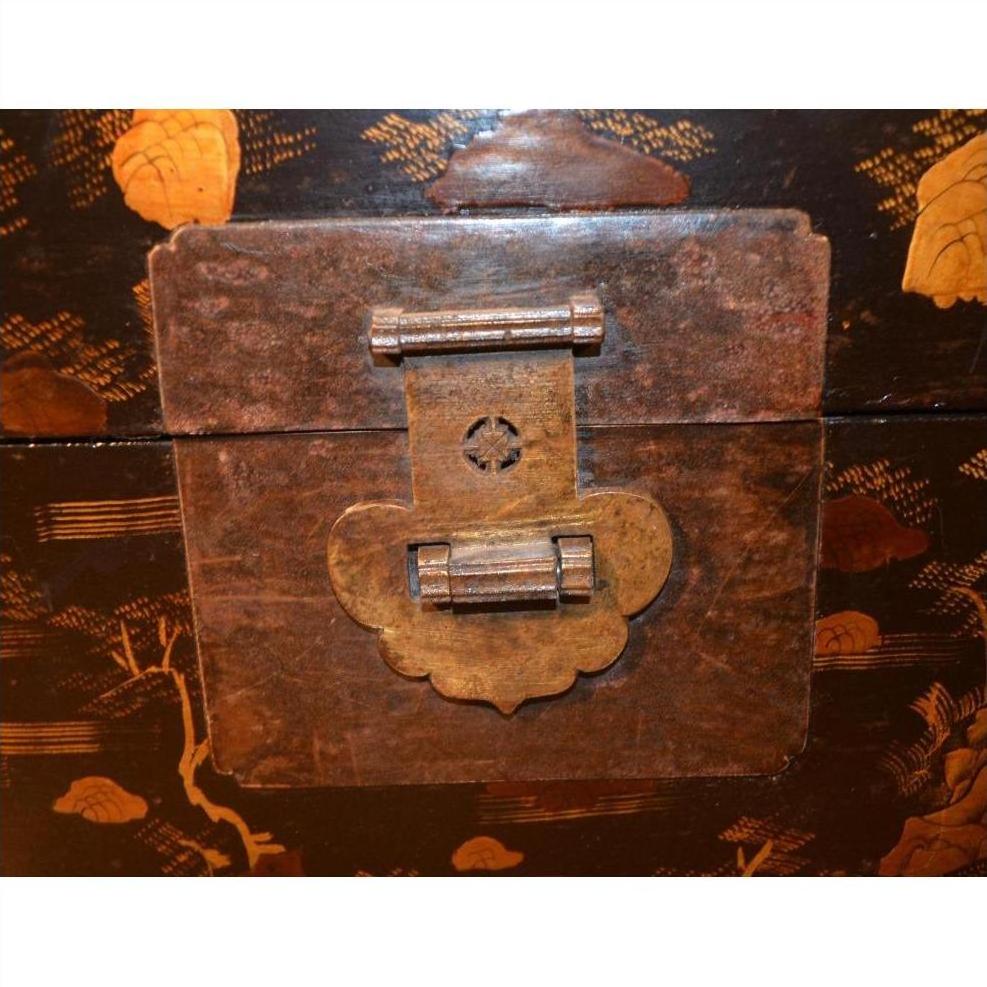 Close-up of an ornate aged brass latch on a black lacquer trunk with gold decorative patterns.