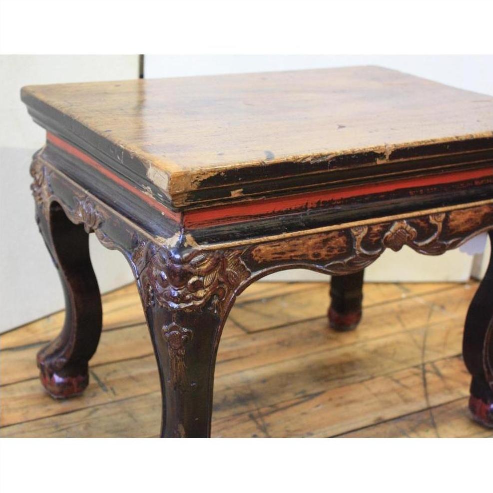 Black lacquered wood side table with ornate carved legs and a worn rectangular top on a wooden floor.