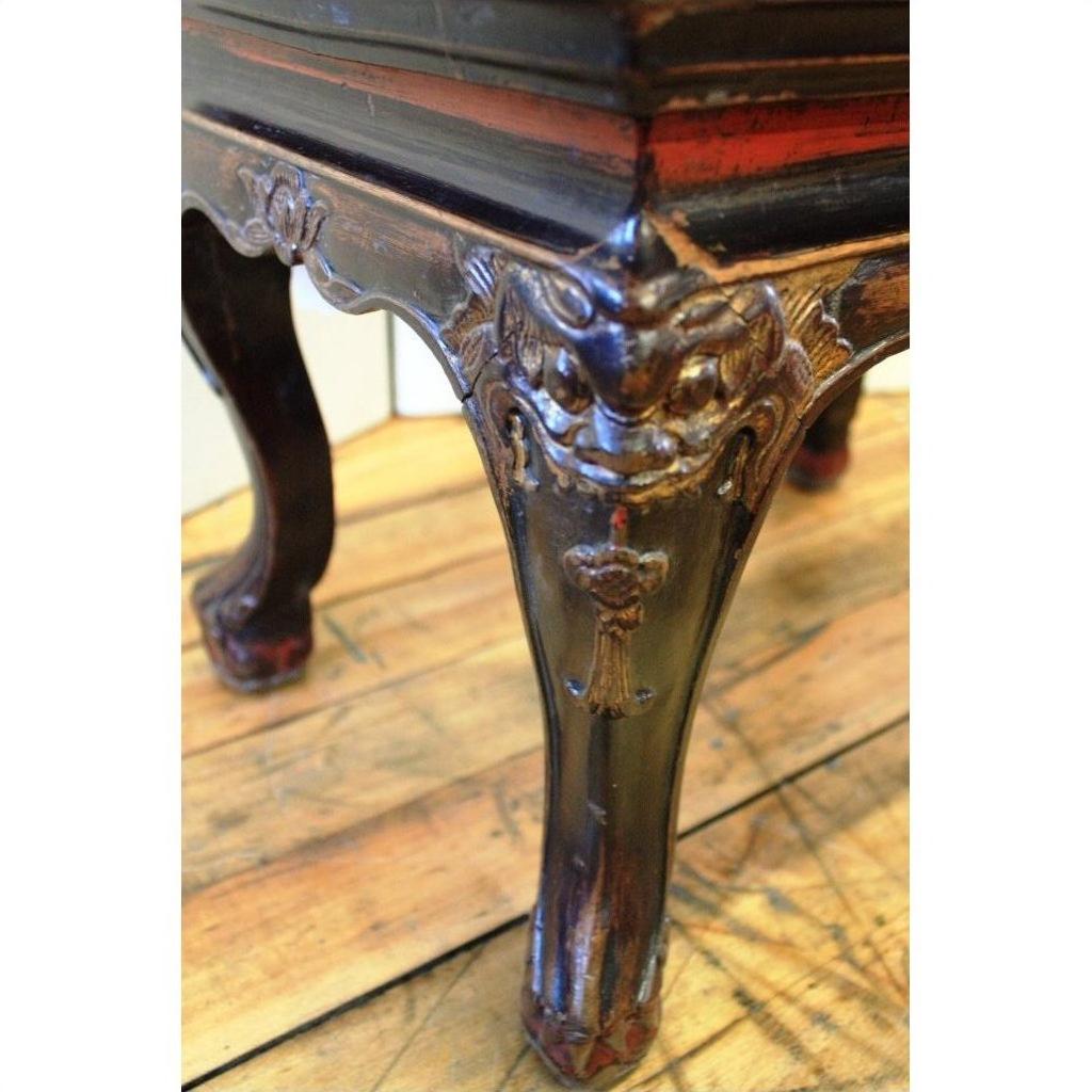 Close-up of black lacquered wood side table leg with carved guardian design on a wooden floor.