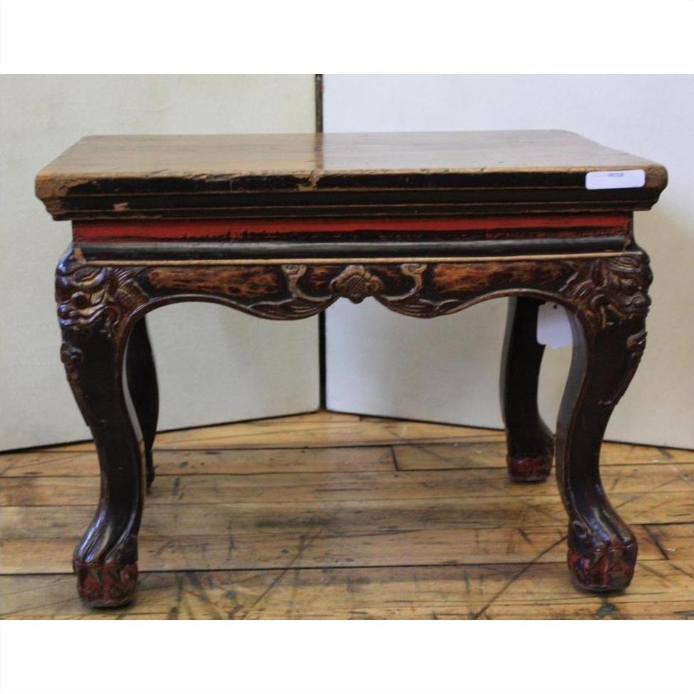 Black lacquered wooden side table with carved guardian design and worn finish, on wooden floor against plain backdrop.