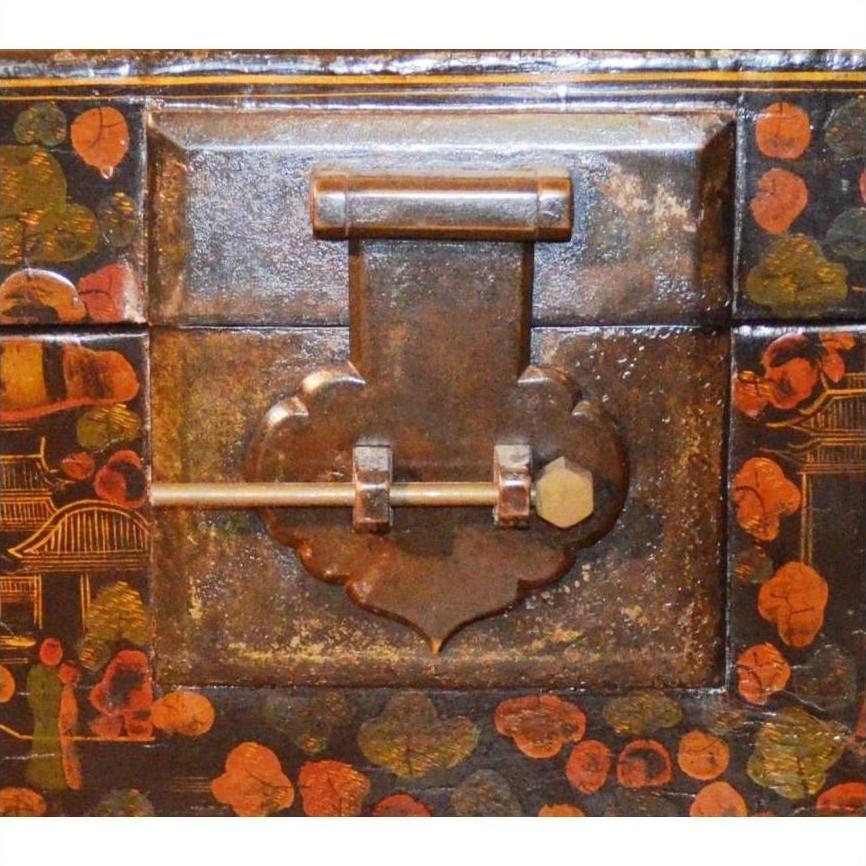 Close-up of decorative metal latch and sliding lock on black lacquered trunk with floral and landscape designs on stand.