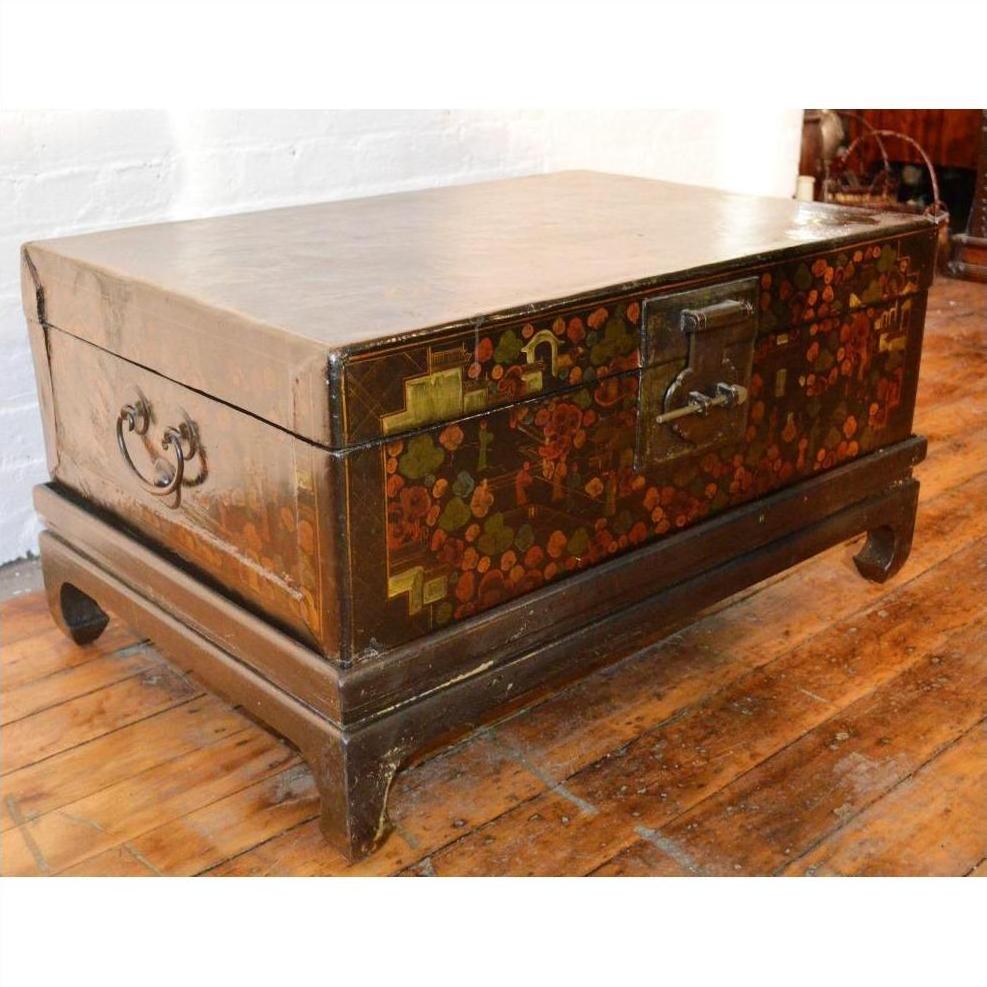 Black lacquered wood trunk with painted floral designs, metal handles, and latch on wooden floor.