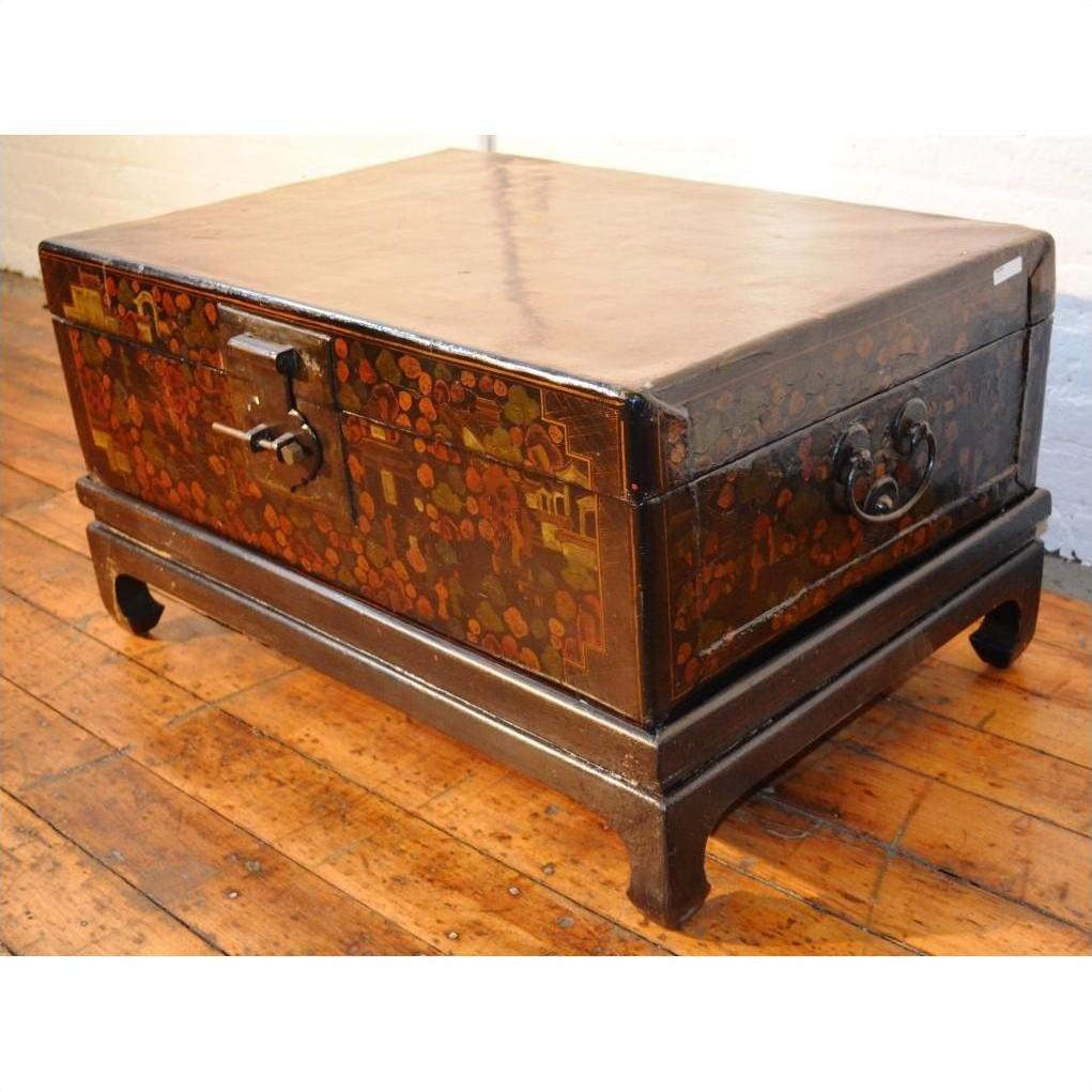 Black lacquered wood trunk with floral designs, metal handles, and lock on stand, placed on a wooden floor.