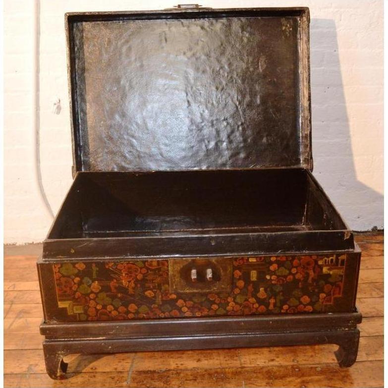 Black lacquered trunk with ornate floral designs on stand, shown on a wooden floor indoors.
