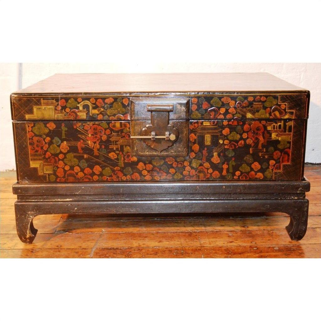 Black lacquered wood trunk with floral designs, metal latch, and raised legs on a wooden floor.