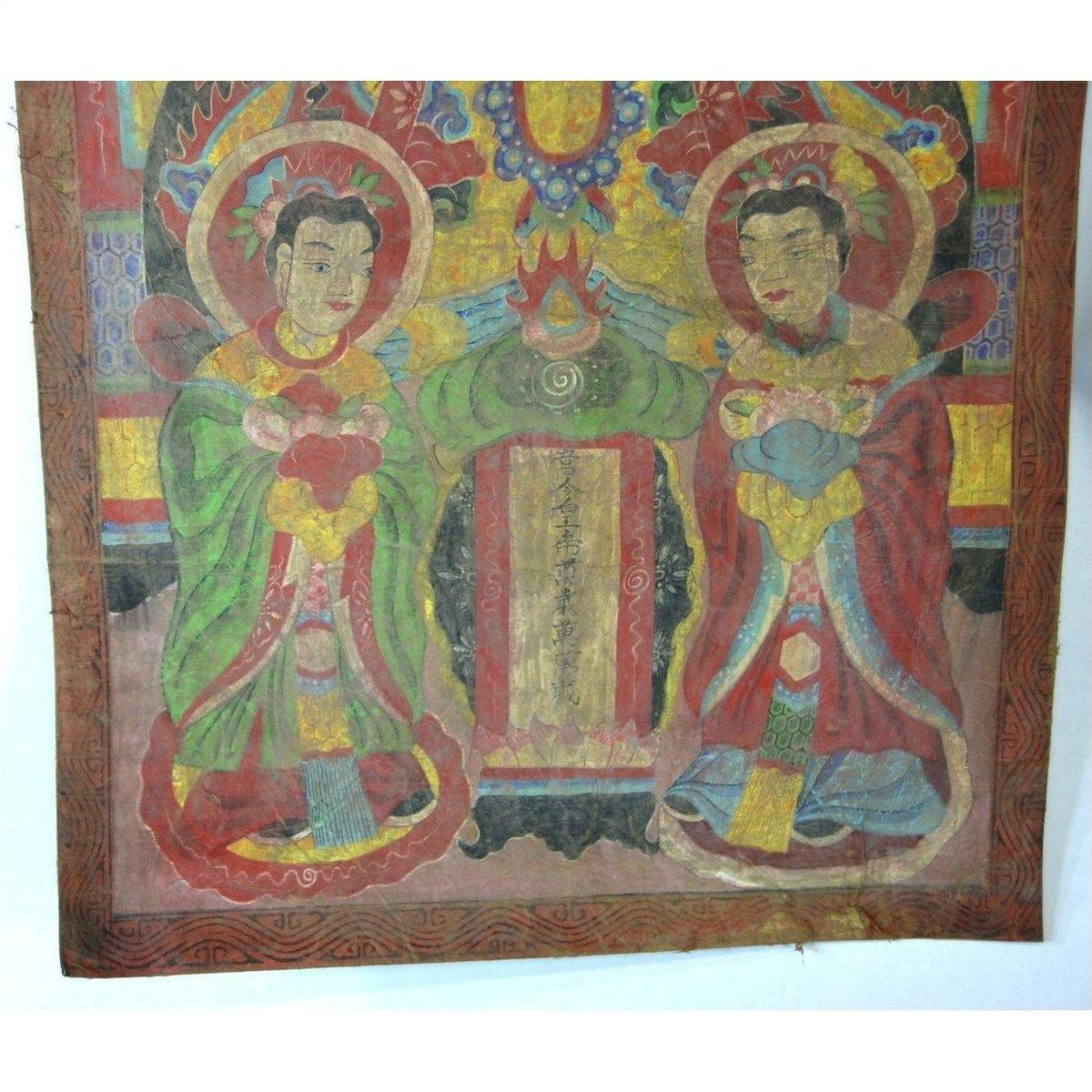 Brown Laotian parchment painting with two haloed figures beside a scroll, double plexiglass frame, close-up view.