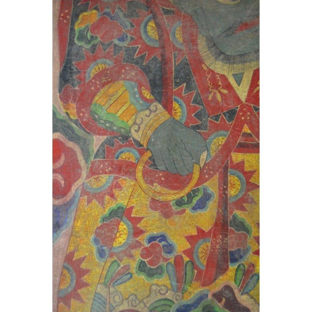 Close-up of a Laotian parchment painting showing a hand with golden ring amid red, yellow, and green patterns.