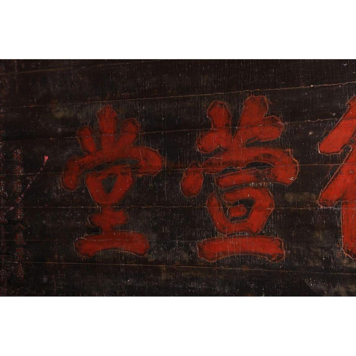 Close-up of a dark wooden 19th century Chinese signboard with red Chinese characters on a worn surface.