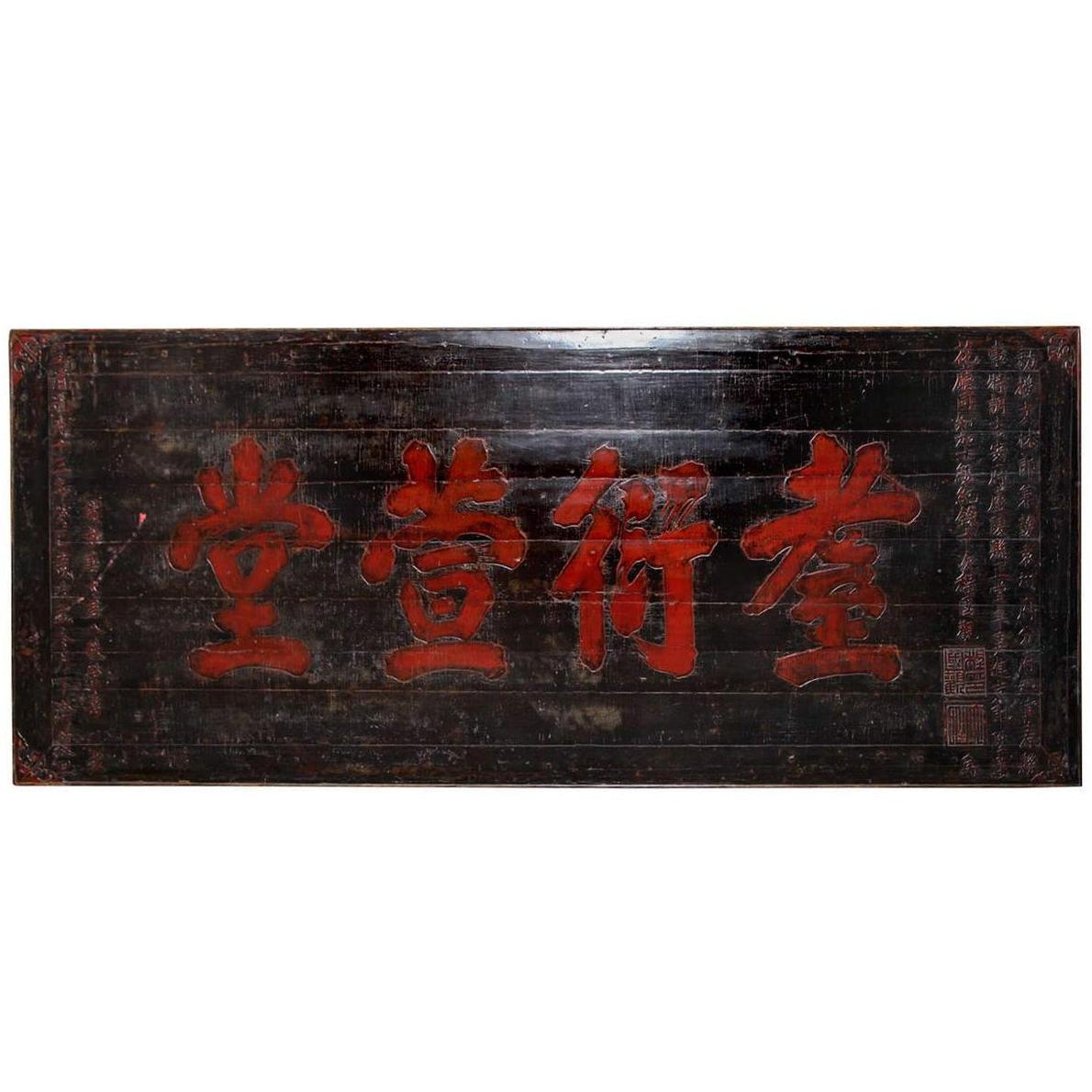 Close-up of a 19th century wooden signboard with large red Chinese characters and smaller text along the right edge.