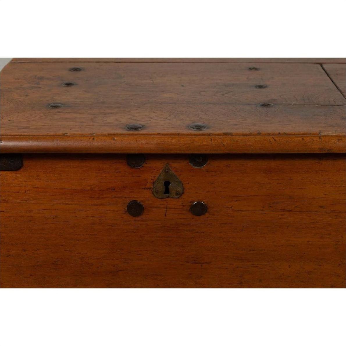 Close-up of a large brown teak wood blanket chest with iron nailheads, keyhole, and wheels.