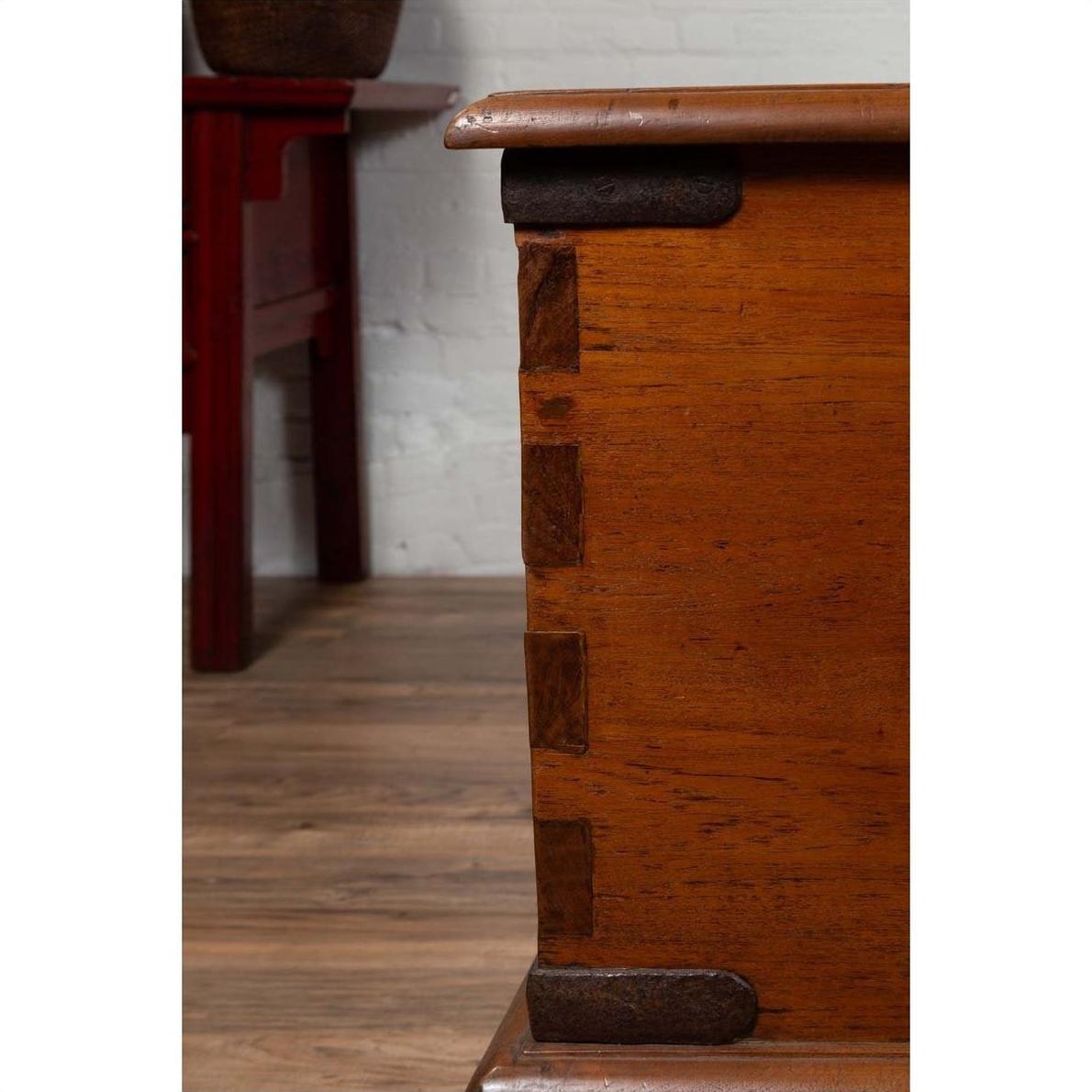 Close-up of brown teak wood blanket chest with iron nailheads and wheels, on a wooden floor.