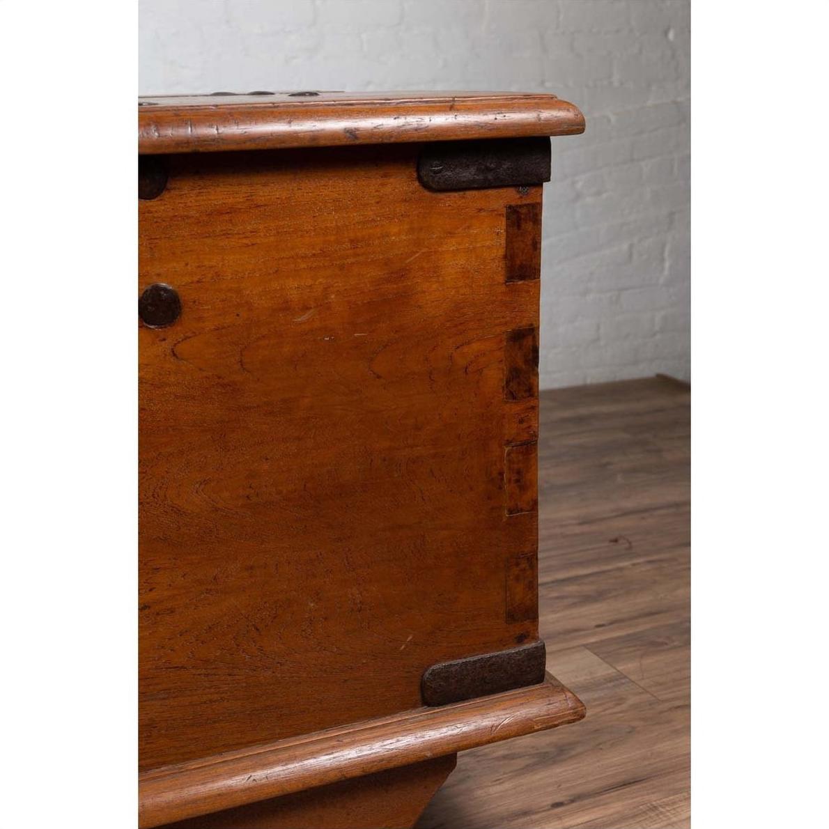Close-up of a large brown teak wood blanket chest with iron nailheads on wheels, on wooden floor indoors.