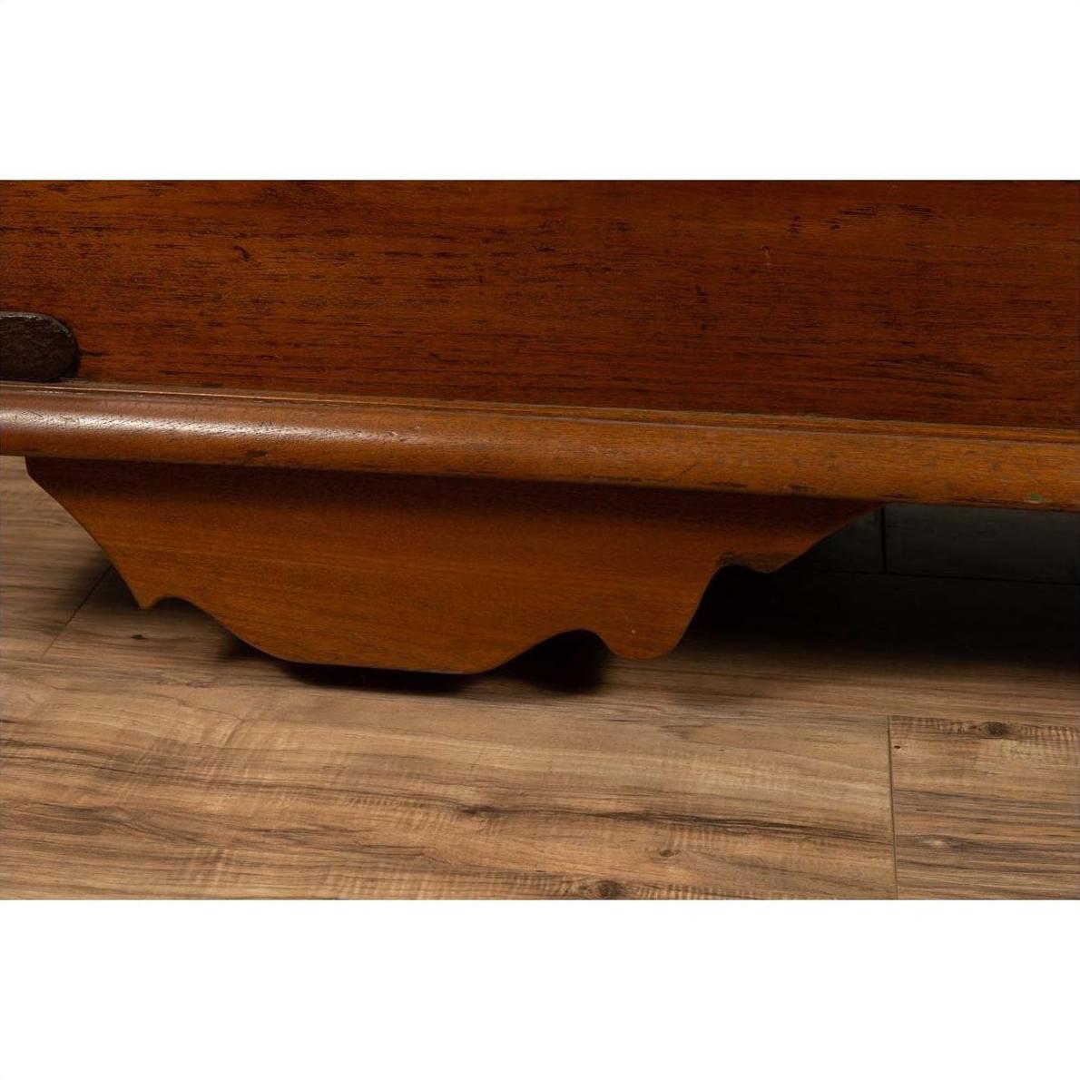 Close-up of brown carved teak wood base with iron nailheads and wheels from a large antique Javanese chest.