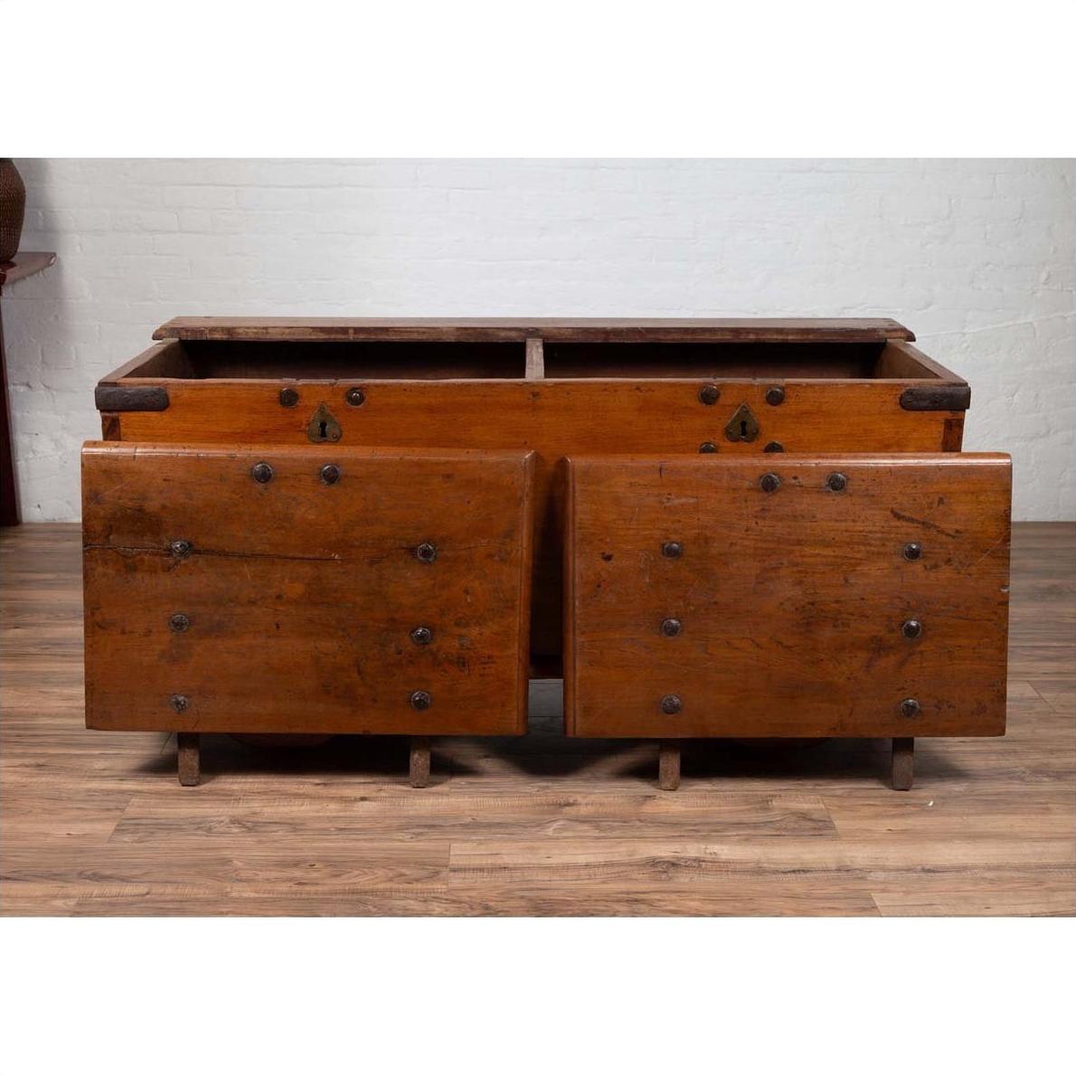 Brown teak wood blanket chest with iron nailheads on wheels, placed on a wooden floor.